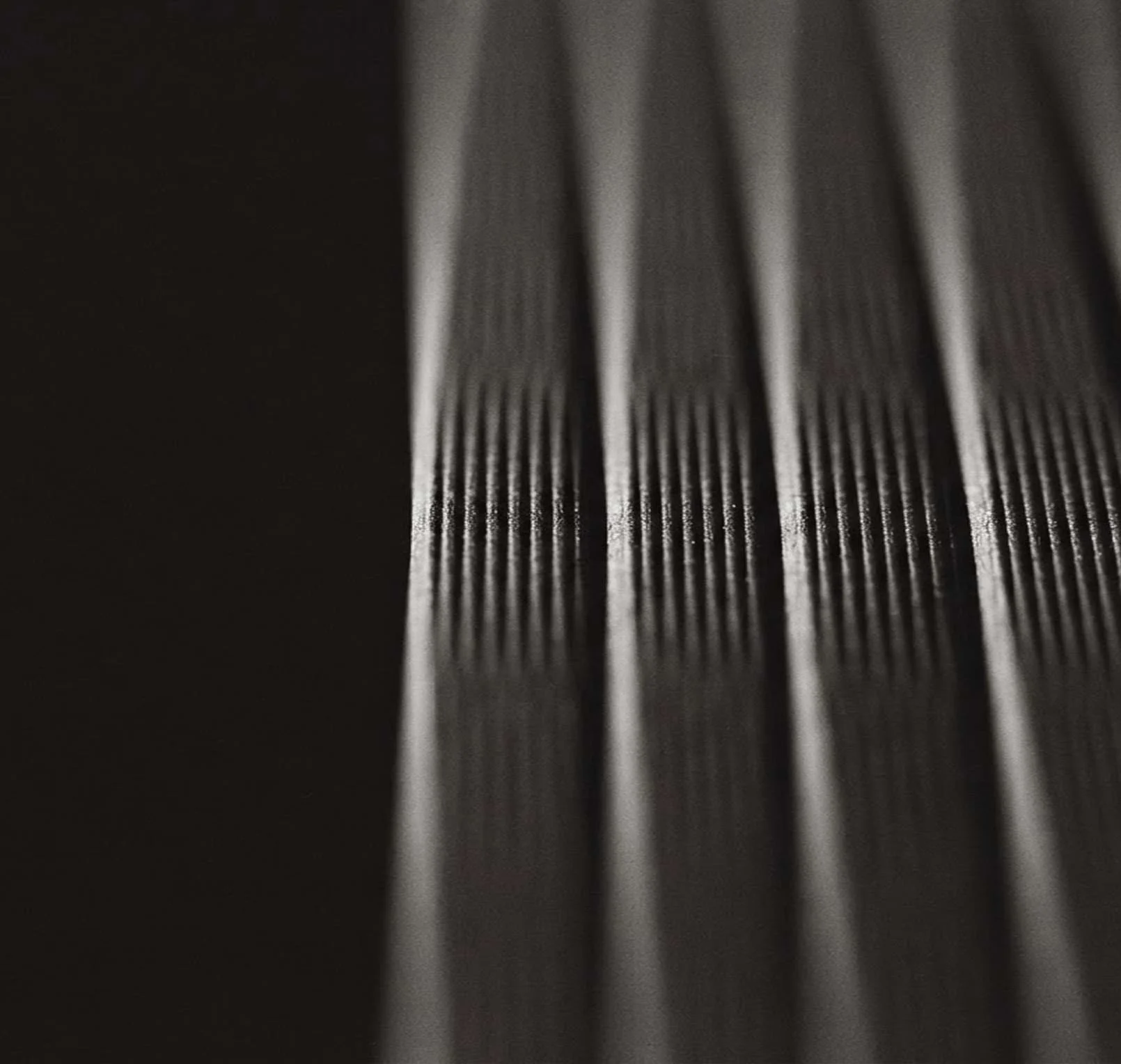 Dark pleated fabric in vertical folds, a band of fine ribbing catching the light across the middle